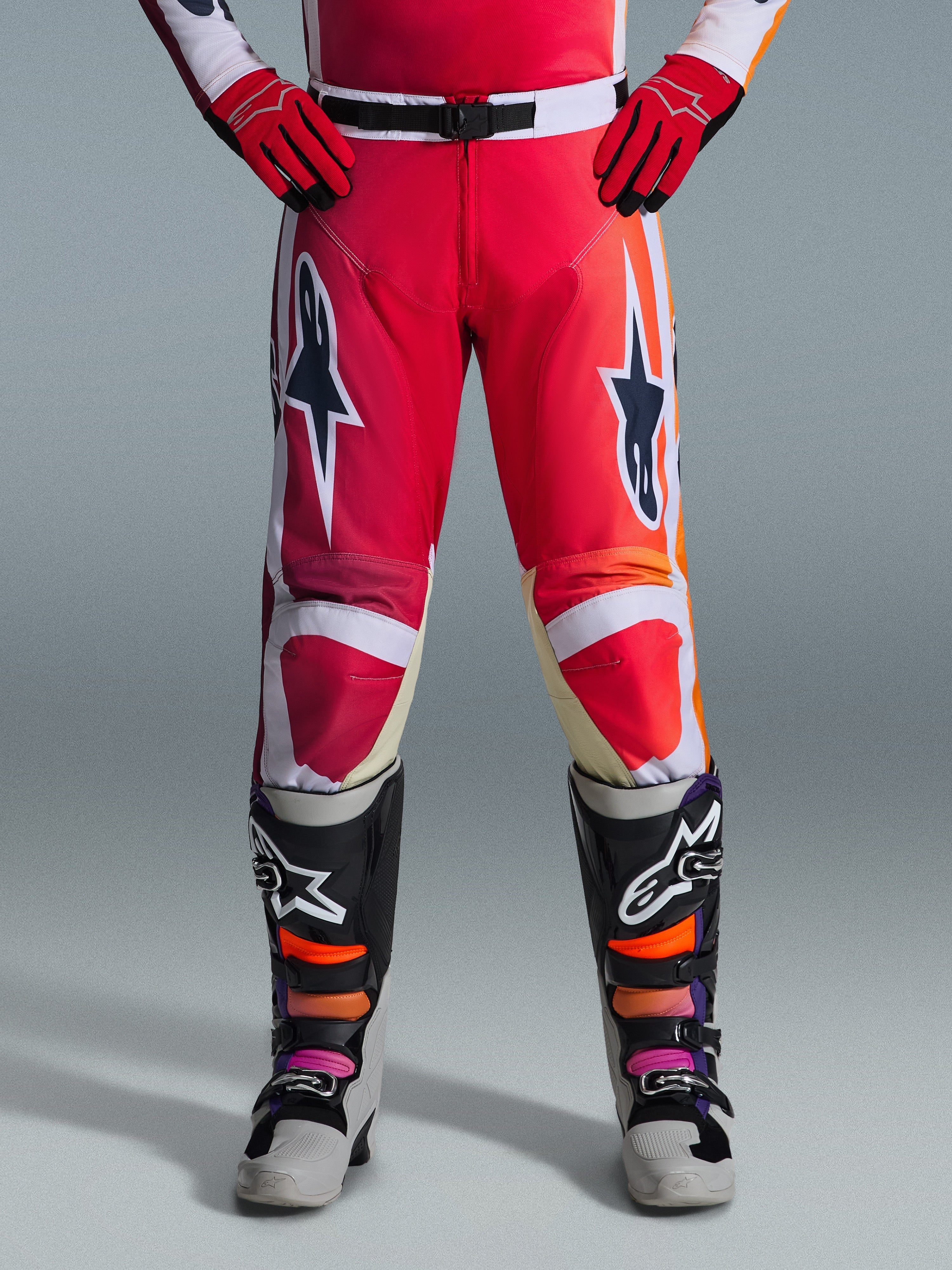 Alpinestars 2026 Racer Portl Pants, pantalon de motocross, rouge, gris clair et gris foncé, porté avec des gants rouges assortis et des bottes multicolores, arborant des logos étoiles Alpinestars sur les cuisses et des détails blancs, design sportif pour la course tout-terrain