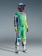 Motorcrossrijder met Alpinestars 2026 Racer Portl-broek en bijpassend shirt in groen, wit en zwart met roze logo-accenten, kleurrijke helm, witte en zwarte racelaarzen en neongroene handschoenen, complete kledingset voor off-road rijden