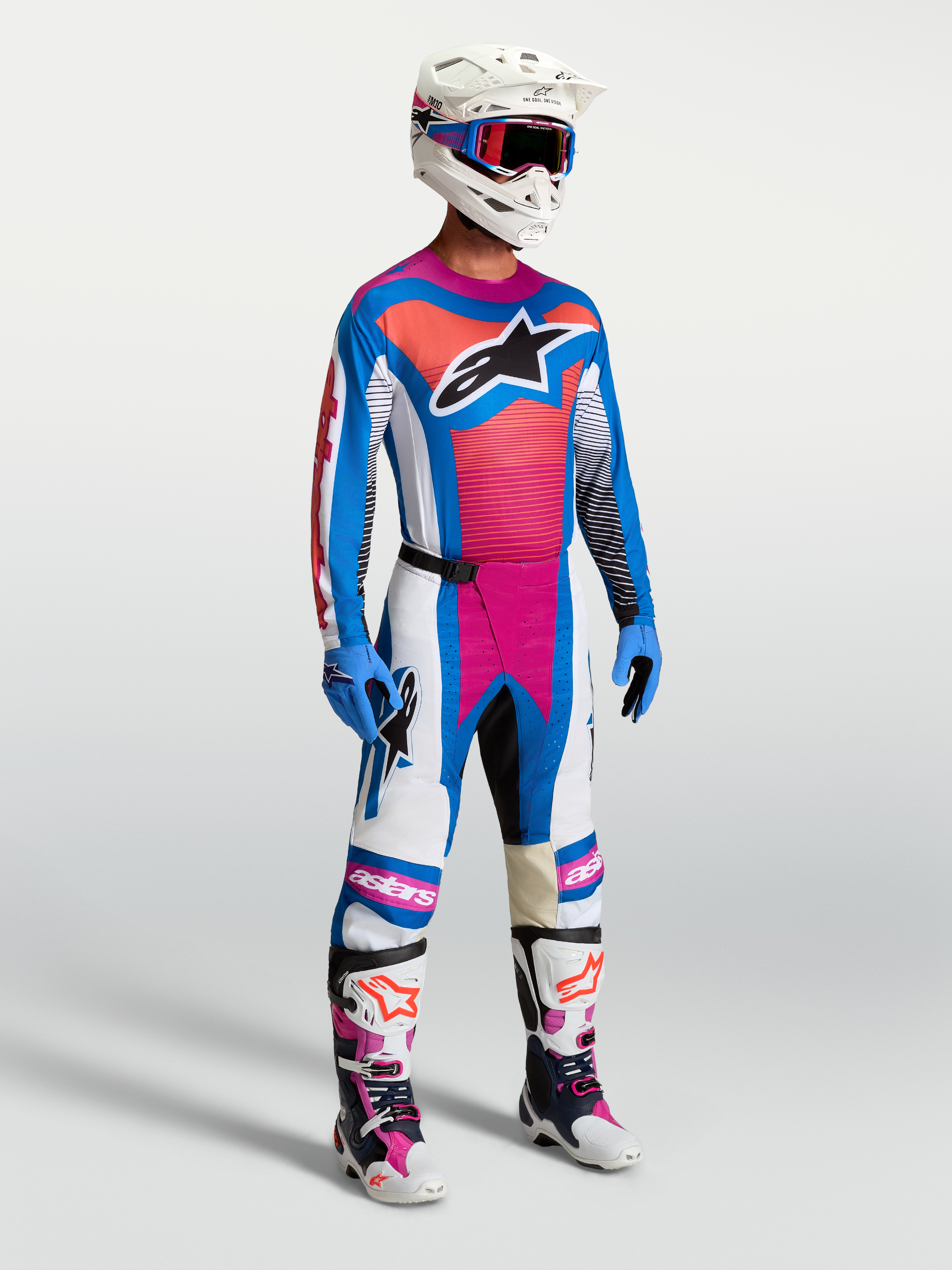 Alpinestars Techstar Maven broek, motorcrossbroek in wit, koraalroze en blauw, getoond op model in complete raceuitrusting.