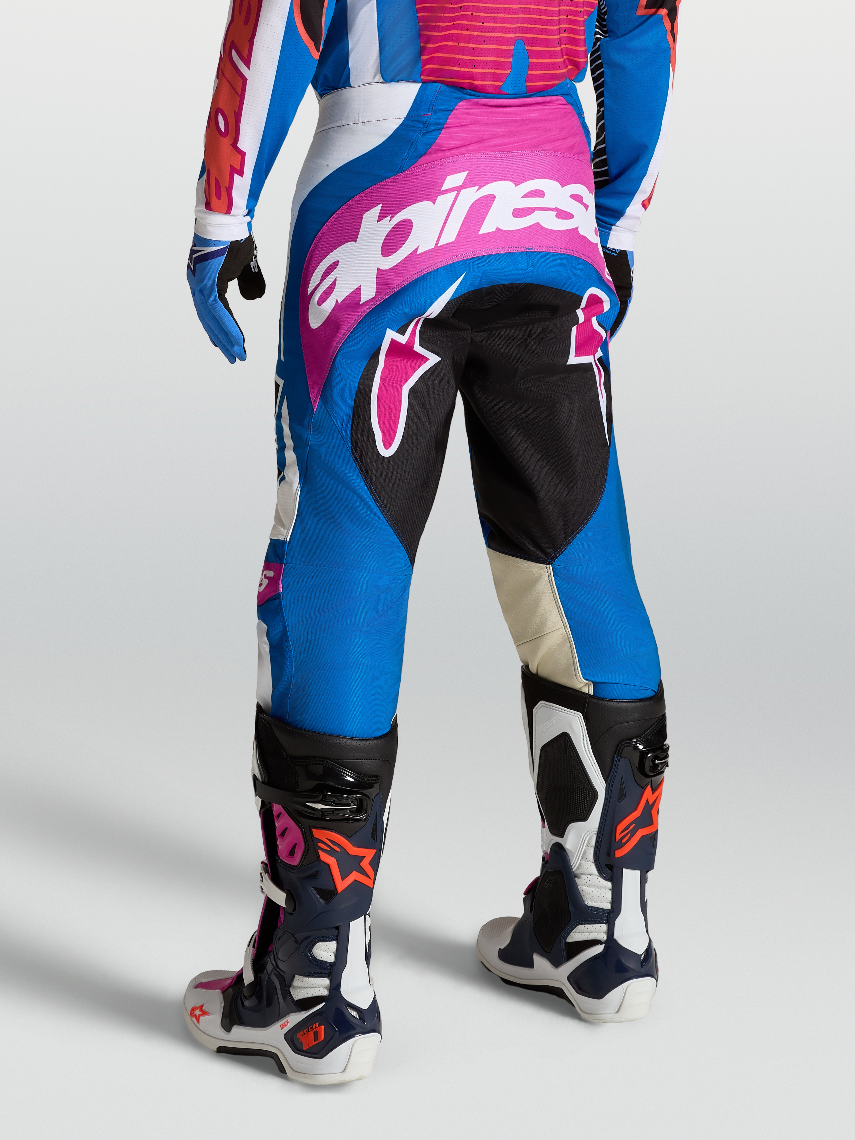 Alpinestars Techstar Maven broek voor heren, motorcrossbroek in blauw en roze, 600D polystof met stretchpanelen, getoond op een model met Tech 10 laarzen, professionele off-road motoruitrusting.