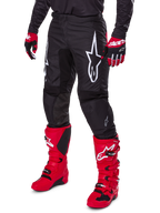 Alpinestars 2025 Fluid Haul Hose, Motocross-Hose, Schwarz, mit großem weißen Alpinestars-Logo, getragen mit leuchtend roten Stiefeln und rot-schwarzen Handschuhen, strapazierfähige 600D-Polygewebe-Konstruktion mit ergonomischem Schnitt für den Offroad-Rennsport