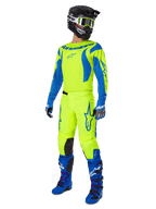 Alpinestars 2025 Fluid Haul crossbroek, motorcross broek, felgeel fluo en blauw, gedragen als onderdeel van een complete race-uitrusting met bijpassend shirt, blauwe laarzen en een zwarte helm, high-visibility ontwerp voor off-road rijden.