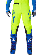 Alpinestars 2025 Fluid Haul motorcrossbroek, felgeel en blauw, gedragen met bijpassende handschoenen en laarzen, zwarte panelen aan de binnenkant van de knieën, opvallende blauwe logo's op de dijen, sportief ergonomisch ontwerp