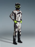 Motocross rider wearing the 2026 Racer Lahnd Jersey in Sand Camo, gray and black camouflage pattern with Alpinestars branding, matching motocross pants, neon yellow gloves, black helmet with yellow goggles, and black boots, complete professional off-road racing outfit.