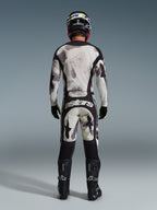 Pilote de motocross vu de dos portant le pantalon Alpinestars Racer Lahnd 2026 en Sand Camo, maillot à manches longues assorti avec motif camouflage gris, bottes de motocross noires, casque noir et marquage « astars » sur l'assise, conçu pour la course tout-terrain professionnelle.