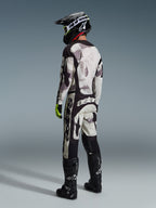 Motocrossrijder in Alpinestars 2026 Racer Lahnd Gear Set, Sand Camo abstract patroon in grijs en wit, zwarte broek met opvallende witte Alpinestars-branding, zwarte helm en laarzen, fluorescerende groene accenten op de handschoenen, complete outfit voor off-road racing
