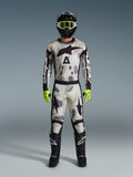 Motocrossrijder in de Alpinestars 2026 Racer Lahnd Gear Set, pak met Sand Camo-patroon in wit, grijs en zwart, zwarte helm met neongroene crossbril, fel neongroene handschoenen en zwarte laarzen met witte logo's, complete gecoördineerde outfit voor off-road racing