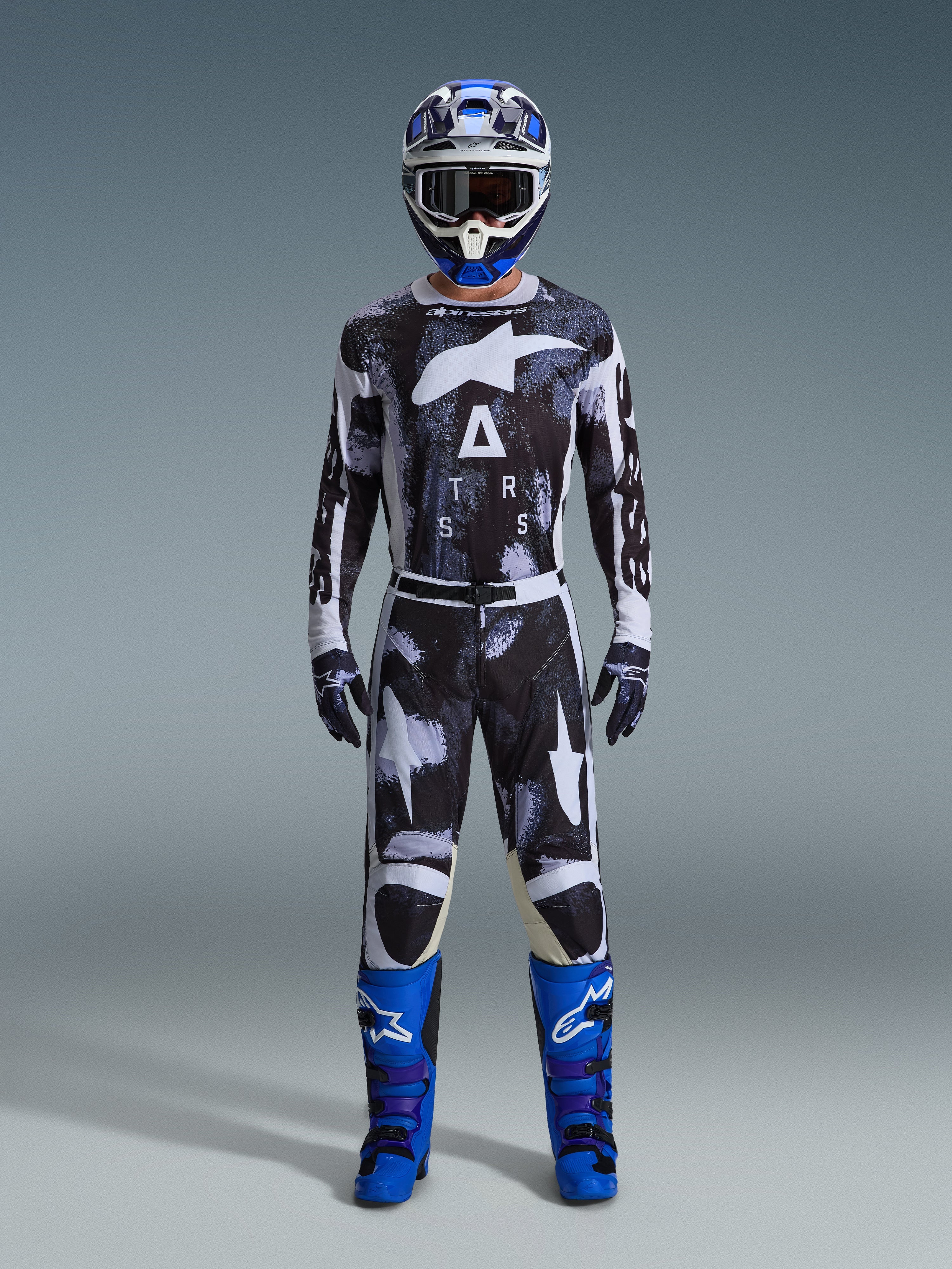 Alpinestars 2026 Racer Lahnd Gear Set, motorcross outfit, zwart en wit met abstract Iron Camo-patroon, gecombineerd met een blauw-witte helm en felblauwe laarzen, complete racekit voor off-road prestaties
