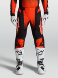 Alpinestars Techstar Swan motocrossbroek 2027 in kardinaalrood en zwart, gestyled met witte motorlaarzen en handschoenen.