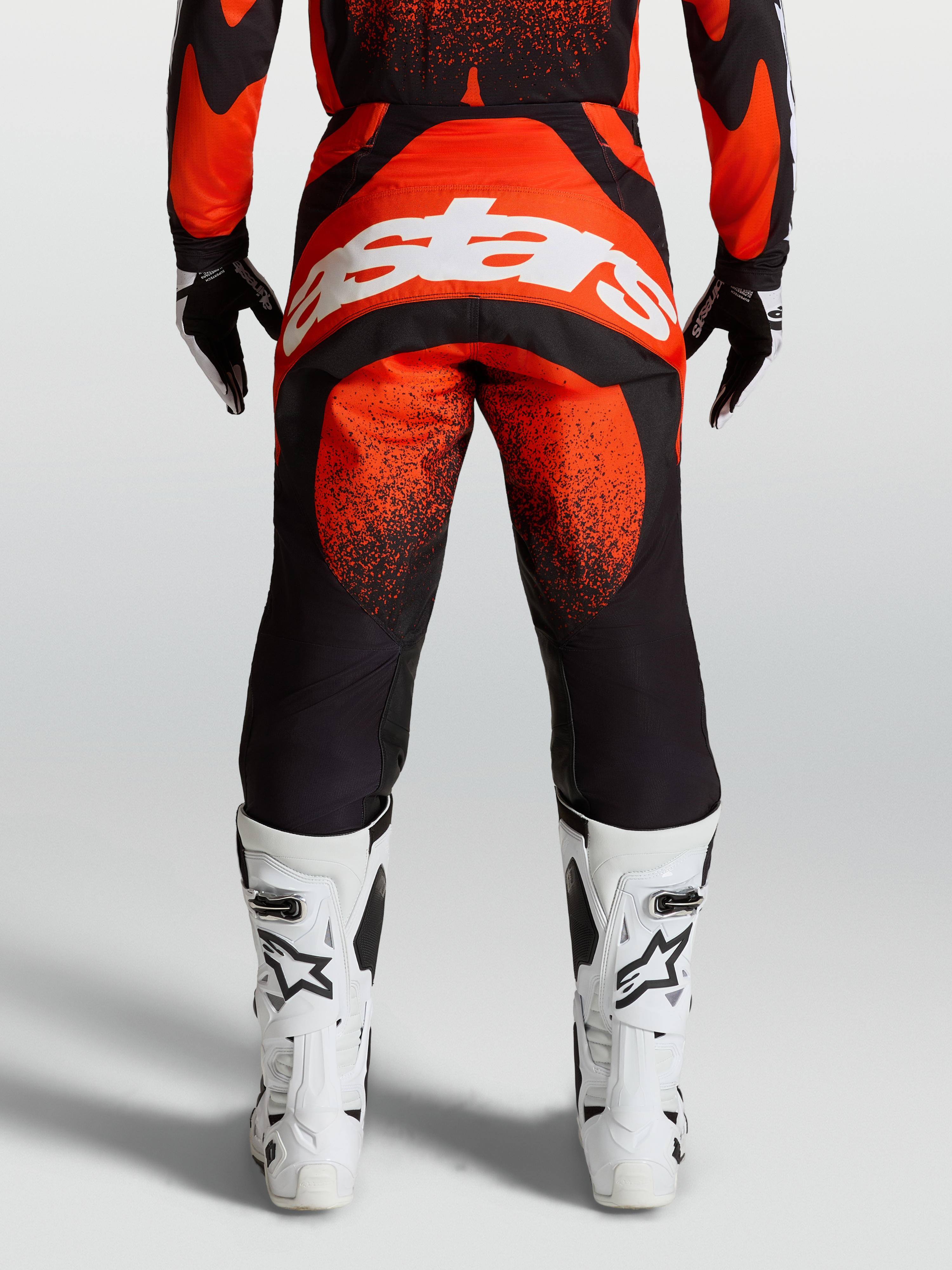 Alpinestars Techstar Swan broek, rode en zwarte motocrossuitrusting, achteraanzicht op model met wit Alpinestars-logo en witte motorlaarzen.