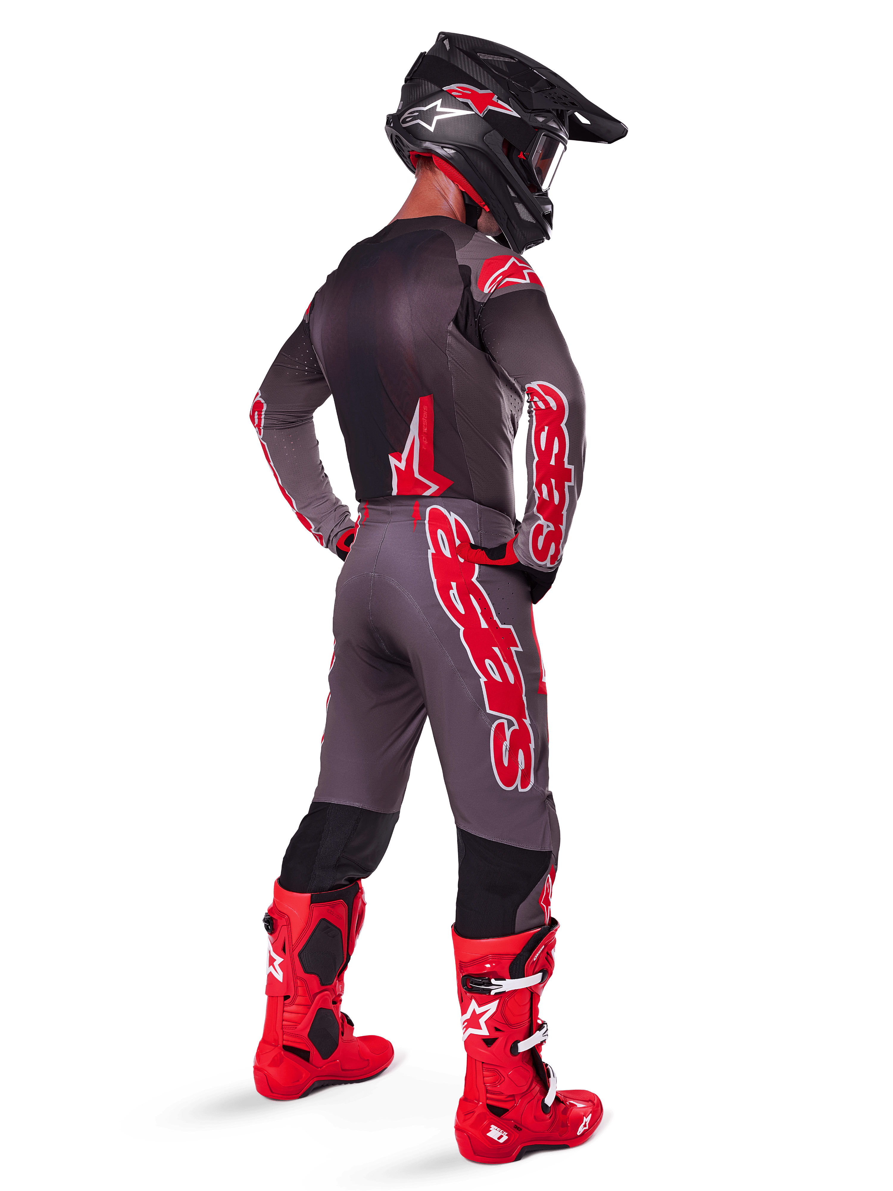 Pilote de motocross portant le pantalon Alpinestars Supertech Lipan 2025, Smoke Bright Red, pantalon gris avec de grands logos rouges et des panneaux intérieurs noirs aux jambes, associé à un maillot gris assorti, un casque noir et des bottes rouge vif, tenue de course tout-terrain complète vue de dos.