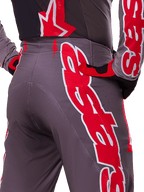 Pantalon Alpinestars Supertech Lipan 2025, pantalon de motocross, rouge vif et gris, gros plan sur la hanche et l'arrière montrant des logos rouges et blancs audacieux, perforations de ventilation, et coupe athlétique de course portée avec la tenue assortie.