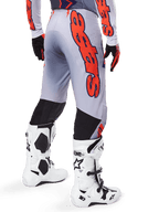 Pantalon Alpinestars Supertech Lipan 2025, pantalon de motocross, gris et orange fluo, porté avec le maillot assorti et des bottes blanches, vue arrière avec grand graphisme Alpinestars orange, empiècements extensibles noirs, équipement de course professionnel