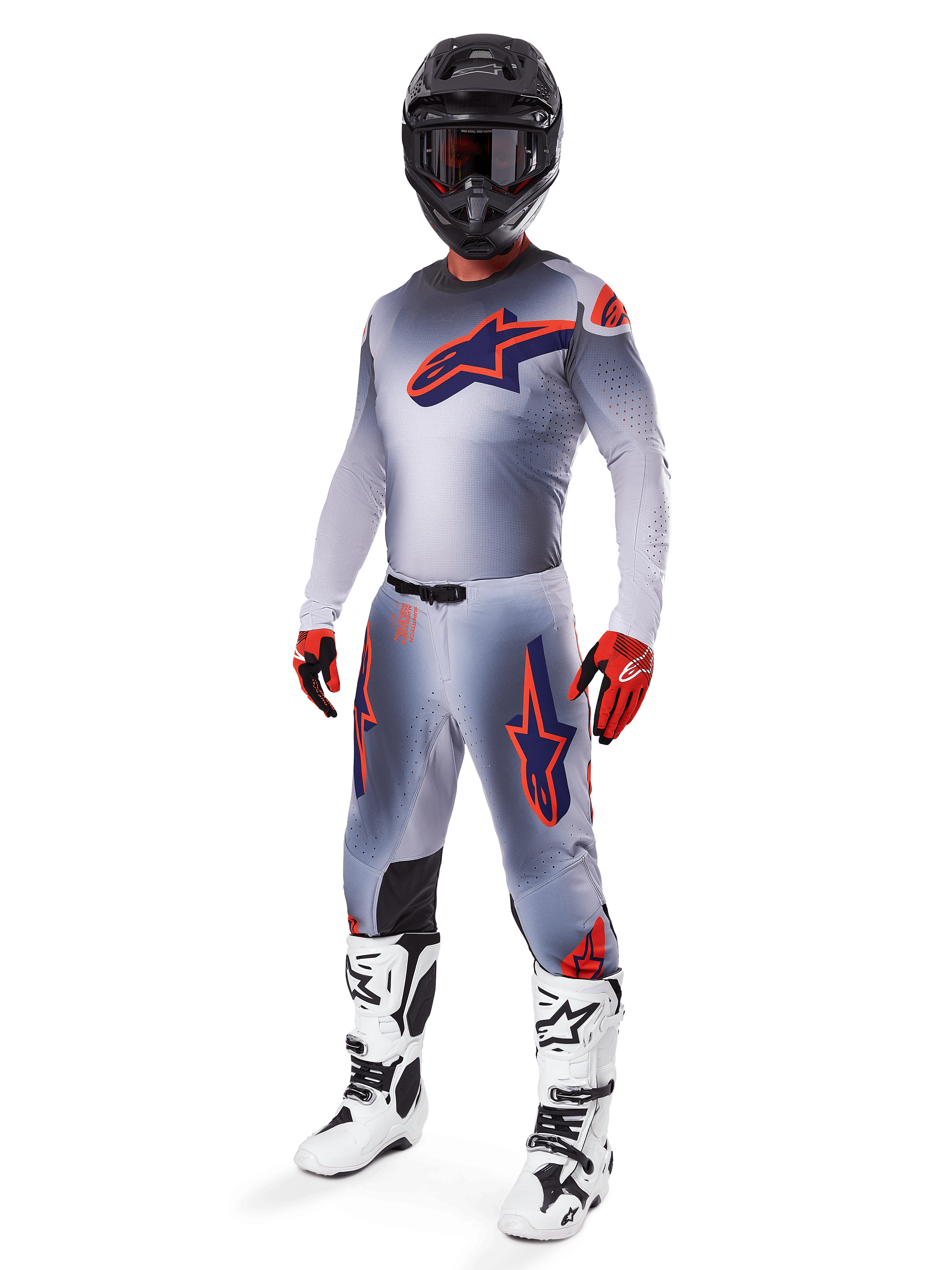 Pilote de motocross portant la tenue de course complète Alpinestars Supertech Lipan 2025, gris et orange fluo, maillot gris avec grand logo orange sur la poitrine, pantalon assorti avec accents orange, casque noir, gants rouges et bottes blanches, équipement de course tout-terrain professionnel