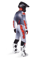 Pilote de motocross vu de dos portant le pantalon Alpinestars Supertech Lipan 2025 en gris et orange fluo, maillot à manches longues assorti, casque noir et bottes techniques blanches et noires, équipement complet de course tout-terrain professionnel.