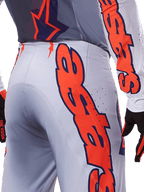 Ensemble maillot et pantalon Alpinestars Supertech Lipan 2025, tenue de motocross, gris et orange fluo, gros plan sur le côté et l'arrière montrant le grand logo Alpinestars orange, tissu ripstop haute performance avec ventilations perforées