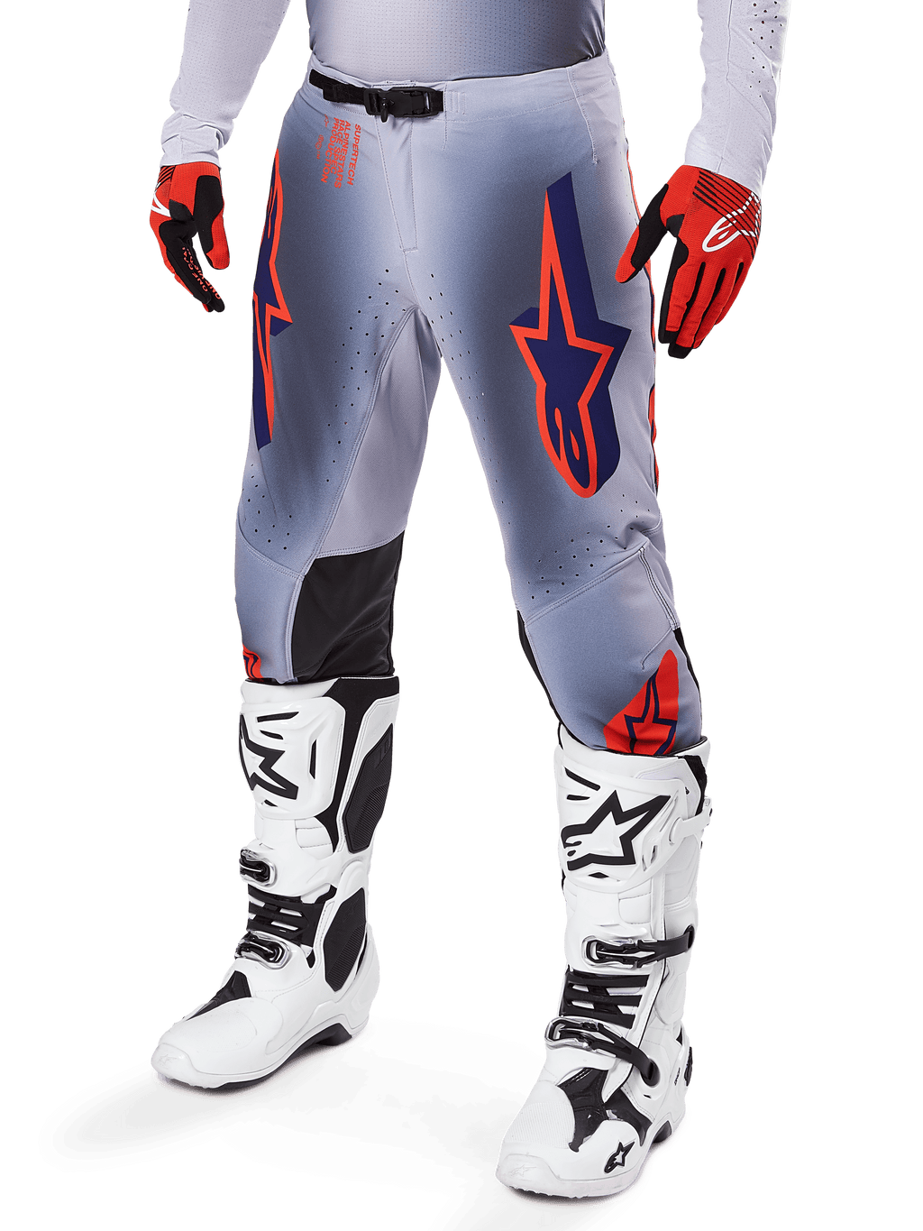 Pantalon Alpinestars Supertech Lipan 2025, pantalon de motocross, gris et orange fluo, avec motifs d'étoiles bleu marine et empiècements noirs à l'intérieur des genoux, porté avec des gants rouge-orange et des bottes blanches, équipement de course tout-terrain professionnel
