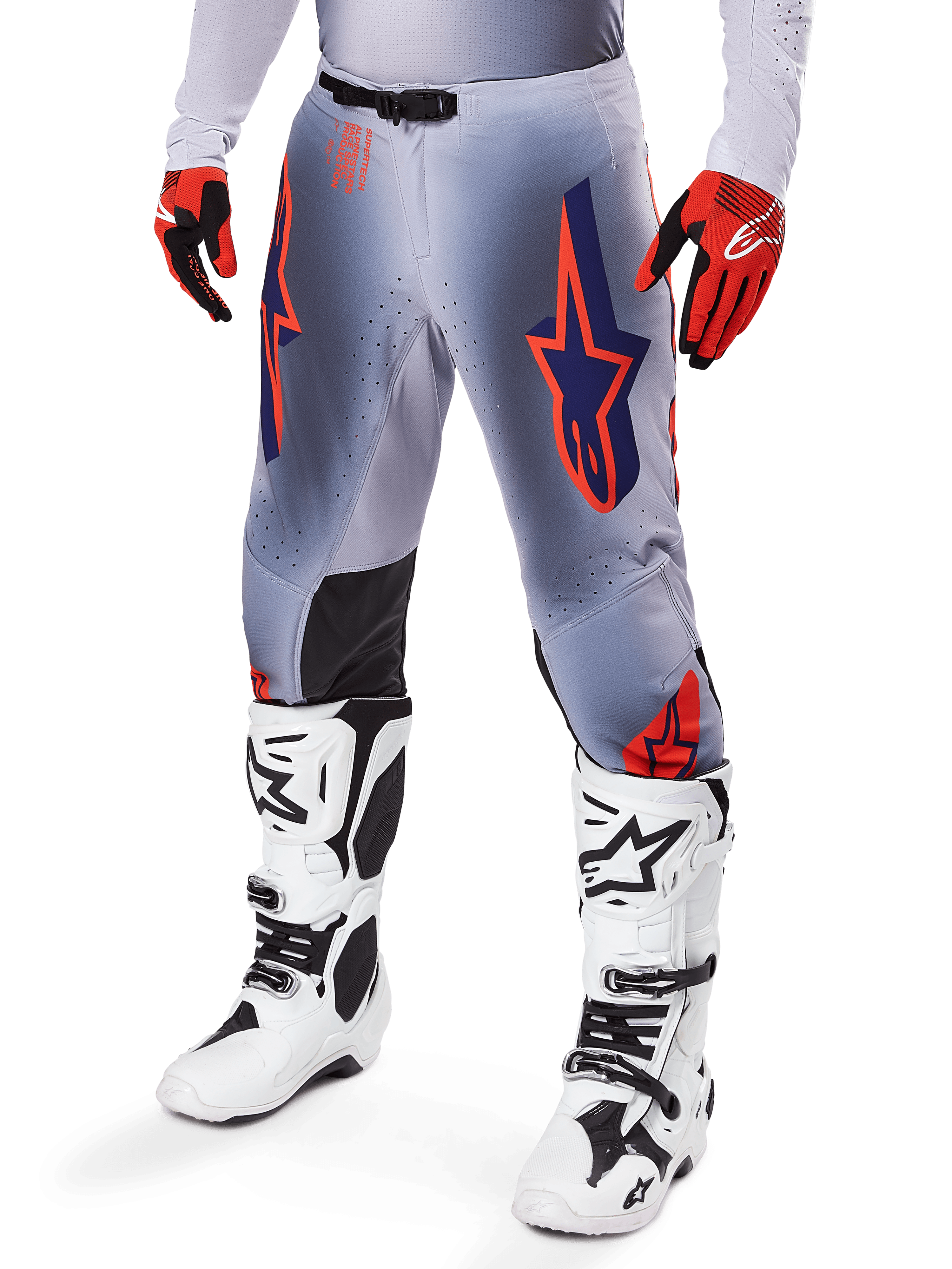 Pantalon Alpinestars Supertech Lipan 2025, pantalon de motocross, gris et orange fluo, avec motifs d'étoiles bleu marine et empiècements noirs à l'intérieur des genoux, porté avec des gants rouge-orange et des bottes blanches, équipement de course tout-terrain professionnel