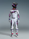 Motocross rider wearing the Alpinestars 2026 Supertech AFD Vista Gear Set, white jersey and pants with pink and purple gradient star graphics, black helmet with matching goggles, white boots with pink accents, and white gloves, coordinated professional off-road racing outfit