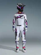 Motocross rider wearing the Alpinestars 2026 Supertech AFD Vista Gear Set, white jersey and pants with pink and purple gradient star graphics, black helmet with matching goggles, white boots with pink accents, and white gloves, coordinated professional off-road racing outfit