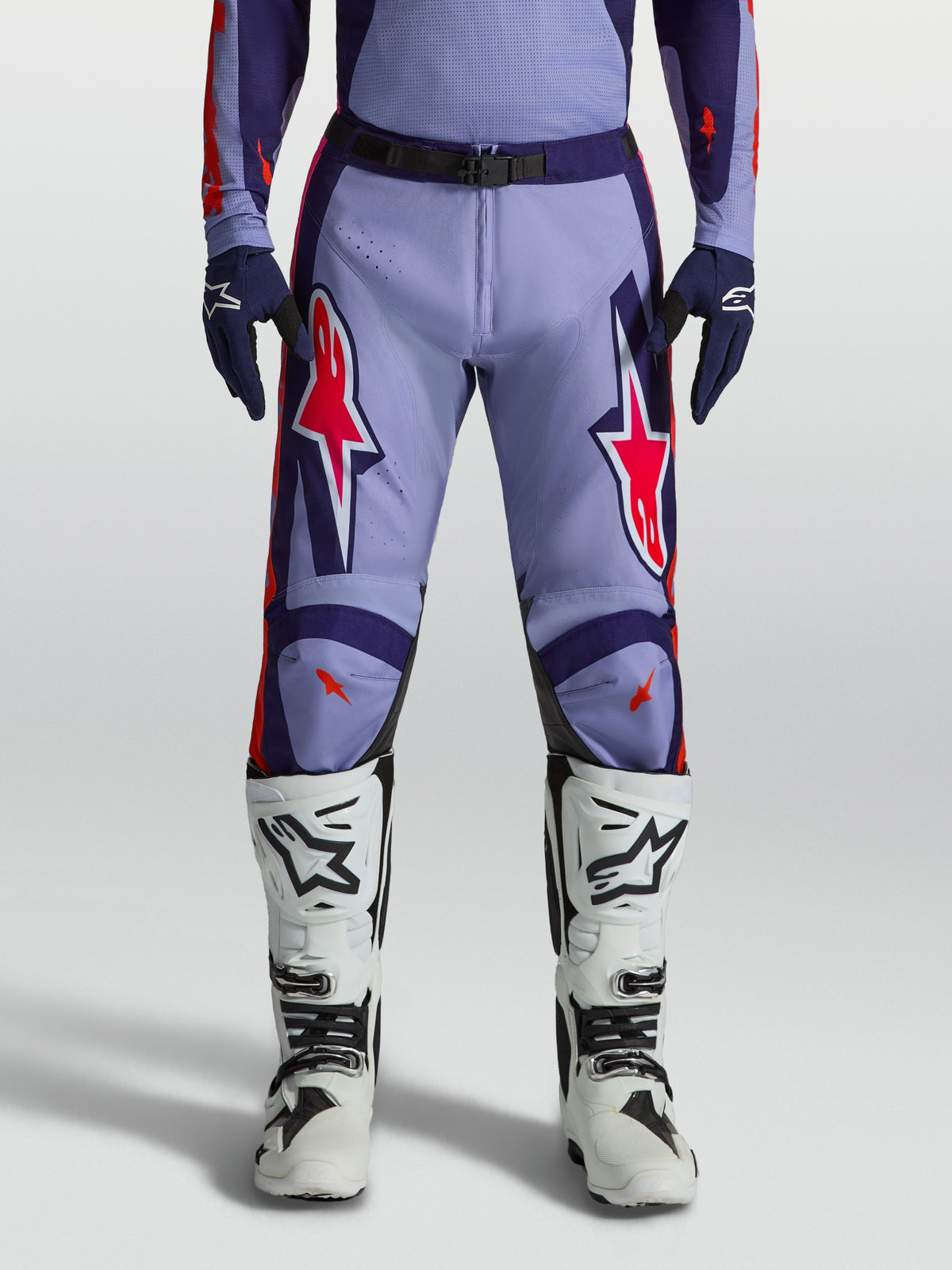 Alpinestars Racer Air Hunt, pantalons de motocross violets et rose fluo, portés avec des bottes blanches
