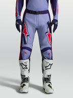 Alpinestars Racer Air Hunt broek, motorcrossbroek voor heren, lichtviolet en paars met roze fluo accenten, gedragen met witte motorlaarzen, geventileerd ontwerp.