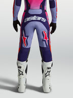 Alpinestars Racer Air Hunt broek, heren-motorcrossbroek in paars en roze, achteraanzicht op model met geventileerde mesh-panelen en witte crosslaarzen.