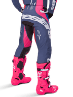 Alpinestars 2025 Techstar Dreem Hose, Motocross-Hose, Grau und Pink mehrfarbig, Rückansicht mit großem weißem Alpinestars-Branding auf dem Gesäß, getragen mit passenden leuchtend pinken Tech 10 Stiefeln, strapazierfähige Offroad-Rennausrüstung mit verstärkten Einsätzen.