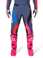 Alpinestars 2025 Techstar Dreem Hose, Motocross-Hose, Grau Mehrfarbig mit blauen, pinken und orangefarbenen Akzenten, getragen mit leuchtend pinken Stiefeln und weiß-schwarzen Handschuhen, mit lasergeschnittenen Perforationen an den Oberschenkeln und einer magnetischen Taillenschnalle, athletische Race-Fit-Ausrüstung für Offroad-Wettbewerbe