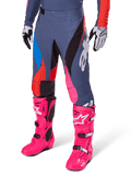 Alpinestars 2025 Techstar Dreem Hose, Motocross-Hose, Dunkelgrau mit blauen, roten und pinken Panels, weiße Grafiken, getragen mit leuchtend pinken Stiefeln und schwarz-weißen Handschuhen, auffälliges High-Visibility-Design