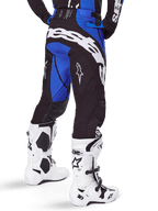 Alpinestars Techstar Dreem Pants 2025, pantalon de motocross, noir et bleu, vue arrière montrant le marquage Alpinestars blanc sur l'assise, porté avec des bottes de motocross blanches et noires et un maillot bleu assorti, coupe athlétique pour la course tout-terrain