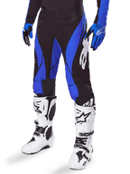 Alpinestars Techstar Dreem Pants 2025, pantalon de motocross noir et bleu, porté avec des bottes de motocross blanches et des gants bleus, avec logo Alpinestars blanc sur la jambe, construction durable pour la course tout-terrain