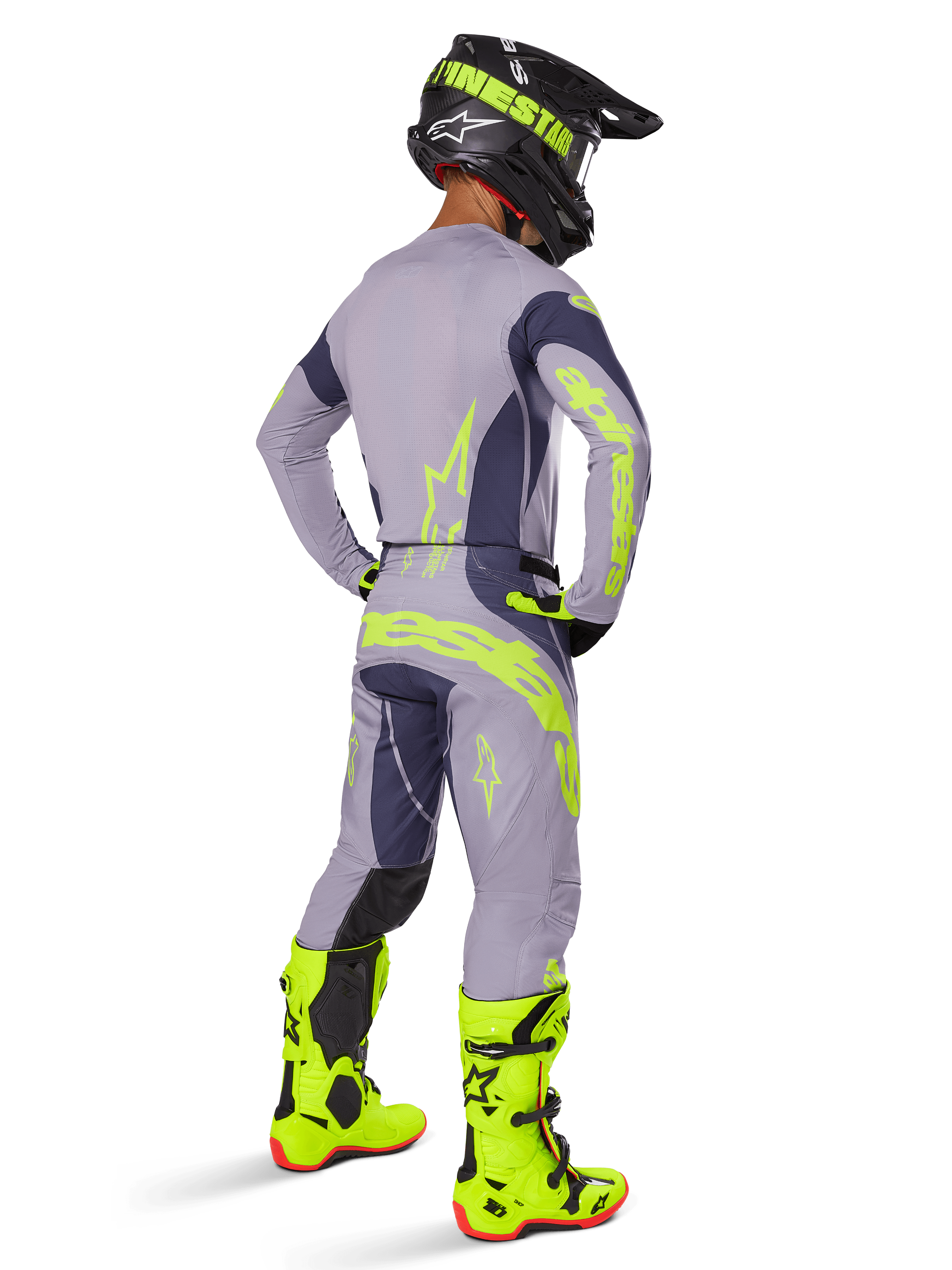 Motocross-Fahrer von hinten gesehen in kompletter Rennausrüstung, Alpinestars 2025 Techstar Dreem Hose in Grau und Dunkelgrau mit auffälligen neongelben Akzenten, passendes graues Trikot mit Neon-Grafiken, leuchtend neongelbe Stiefel und schwarzer Helm, professionell abgestimmtes Motocross-Outfit