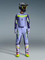 Alpinestars 2026 Supertech Scenz Hose, Motocross-Hose, Purple Yellow Fluo, getragen als komplettes Rennbekleidungsset mit passendem lavendelfarbenem Trikot, Handschuhen und Stiefeln, mit markanten neongelben Logos, athletische Passform für professionellen Offroad-Rennsport.
