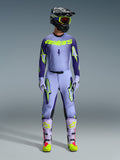 Alpinestars 2026 Supertech Scenz Gear Set, Motocross-Rennoutfit, Hellviolett und Neongelb-grün, komplette Schutzausrüstung, schwarzer Helm mit violetten Akzenten, Jersey mit auffälligem neongelbem Branding, passende Hose mit Stern-Grafiken, abgestimmte Stiefel mit rosa Highlights.