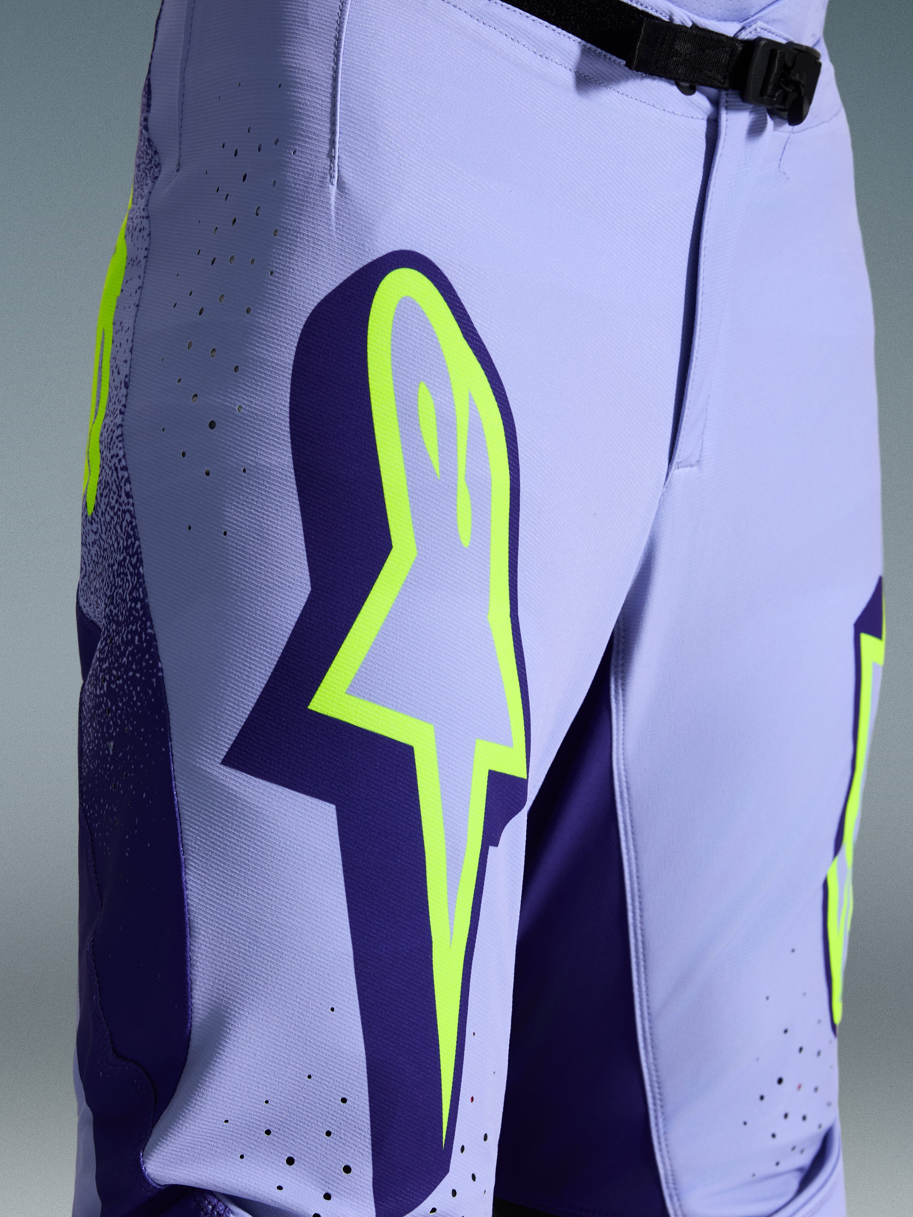 Alpinestars 2026 Supertech Scenz Hose, Motocross-Hose, Lila und Fluo-Gelb, Nahaufnahme mit großem gelben Logo auf dem Oberschenkel, lasergeschnittenen Perforationen zur Belüftung und magnetischem Bundverschluss, sportliche Offroad-Ausrüstung