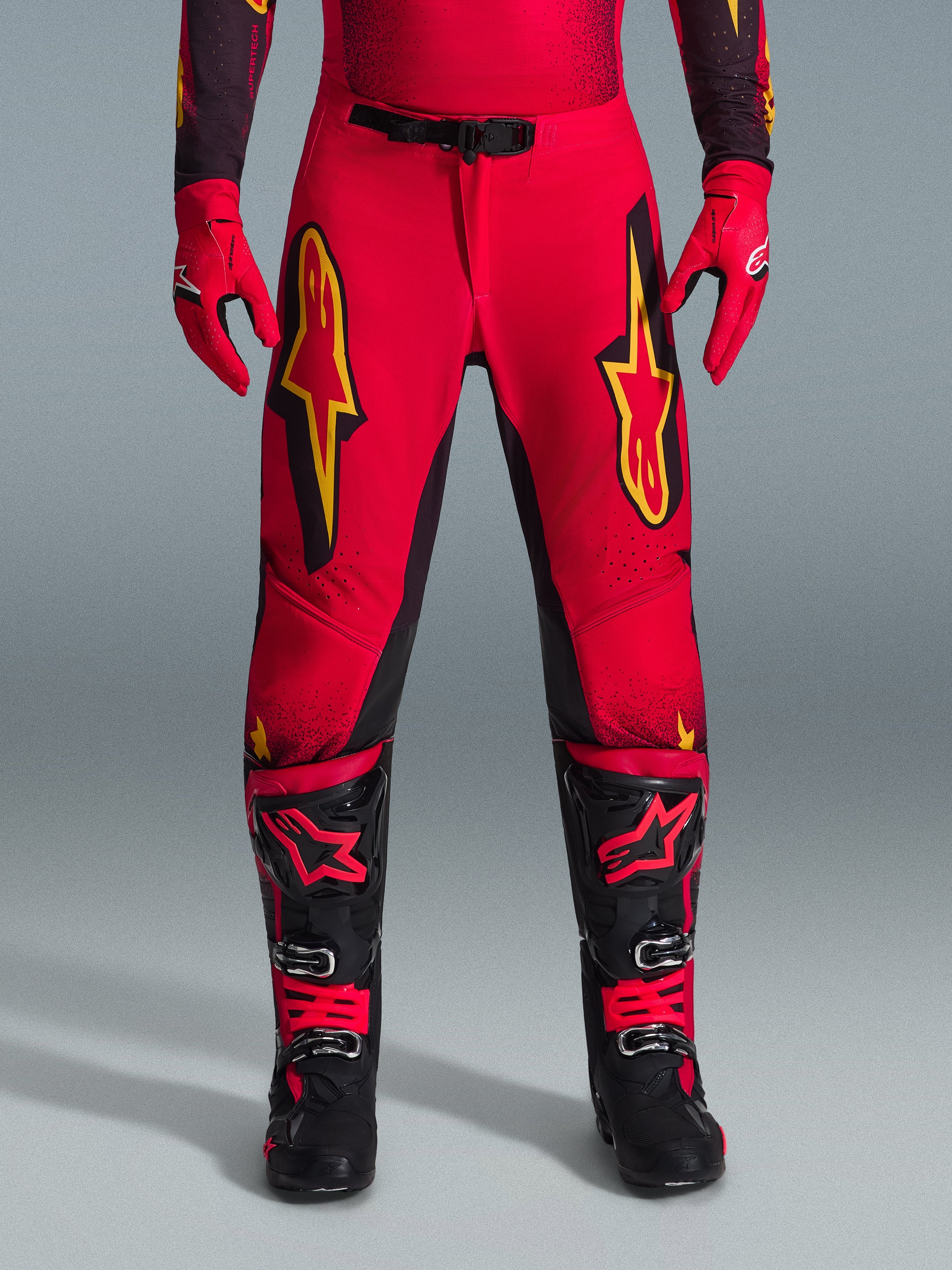 Alpinestars Supertech Scenz 2026, pantalon de motocross, rouge, noir et jaune, coupe athlétique professionnelle avec de grands logos étoiles jaunes sur les cuisses, associé à des gants rouges et des bottes techniques noires et rouges, conçu pour la performance d'élite en tout-terrain