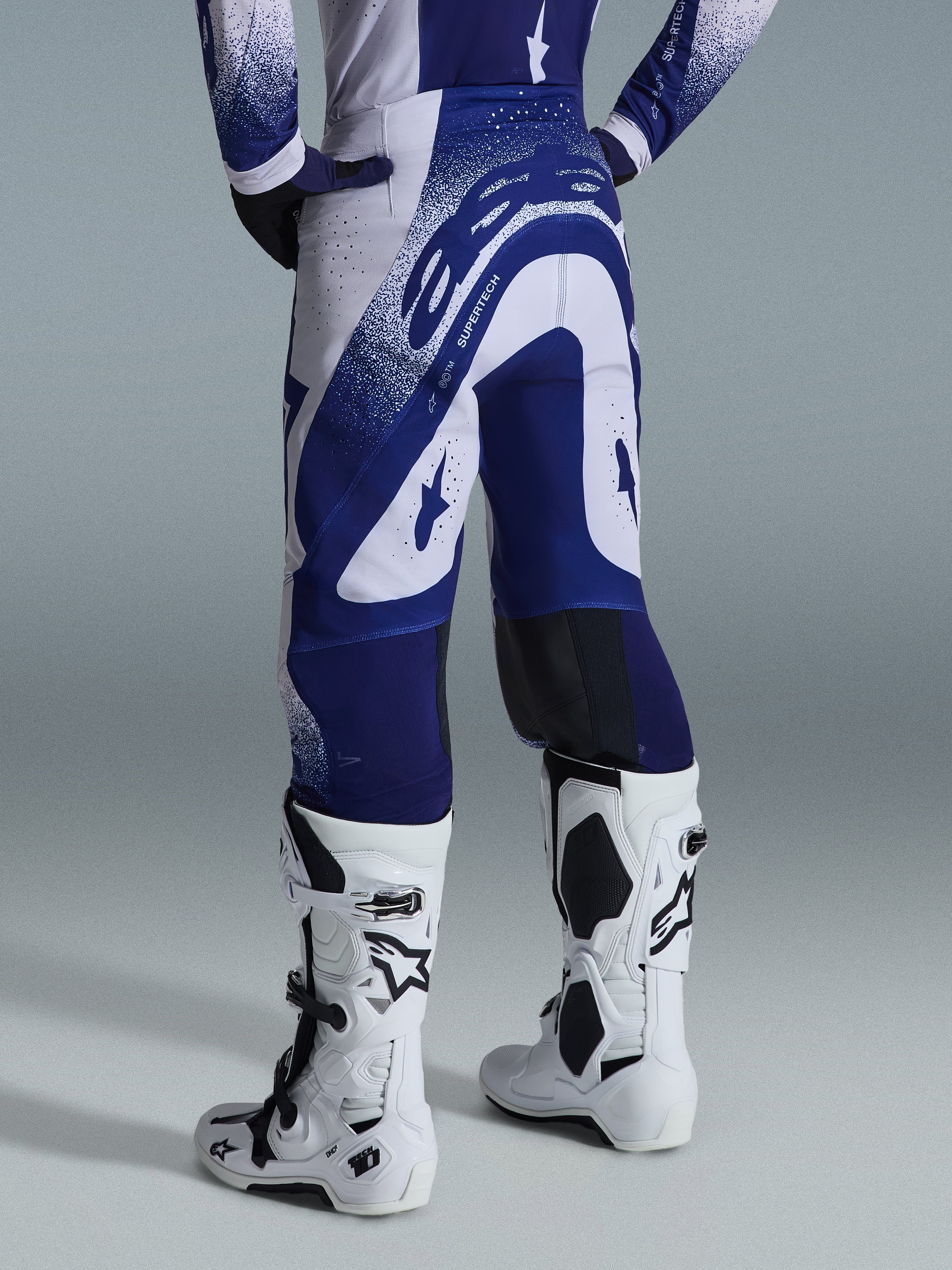 Alpinestars 2026 Supertech Scenz Pants, Motocross Pants, Light Gray and Dark Blue, rear view worn with matching jersey and white boots, featuring bold blue graphics with speckled accents, performance athletic fit for off-road racing.