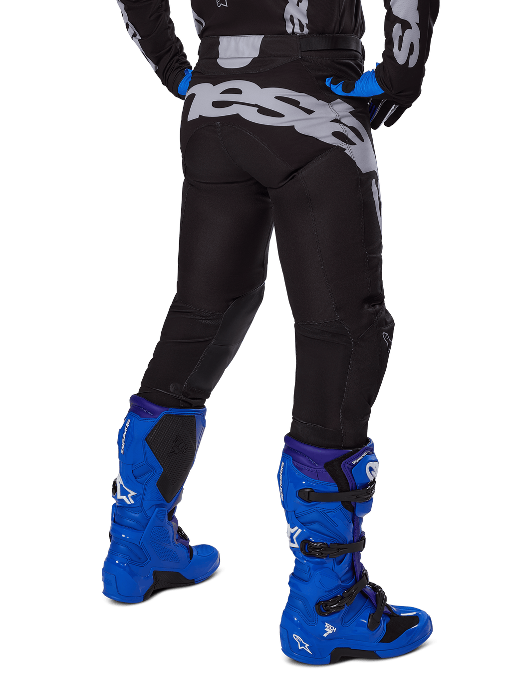 Alpinestars 2025 Racer Graphite Pants, pantalon de motocross, noir et gris, vue arrière avec un grand logo gris sur l'assise, porté avec des bottes de motocross bleu vif et un maillot noir et bleu, équipement de course tout-terrain durable