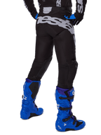 Alpinestars 2025 Racer Graphite Pants, pantalon de motocross, noir et gris, vue arrière avec un grand logo gris sur l'assise, porté avec des bottes de motocross bleu vif et un maillot noir et bleu, équipement de course tout-terrain durable