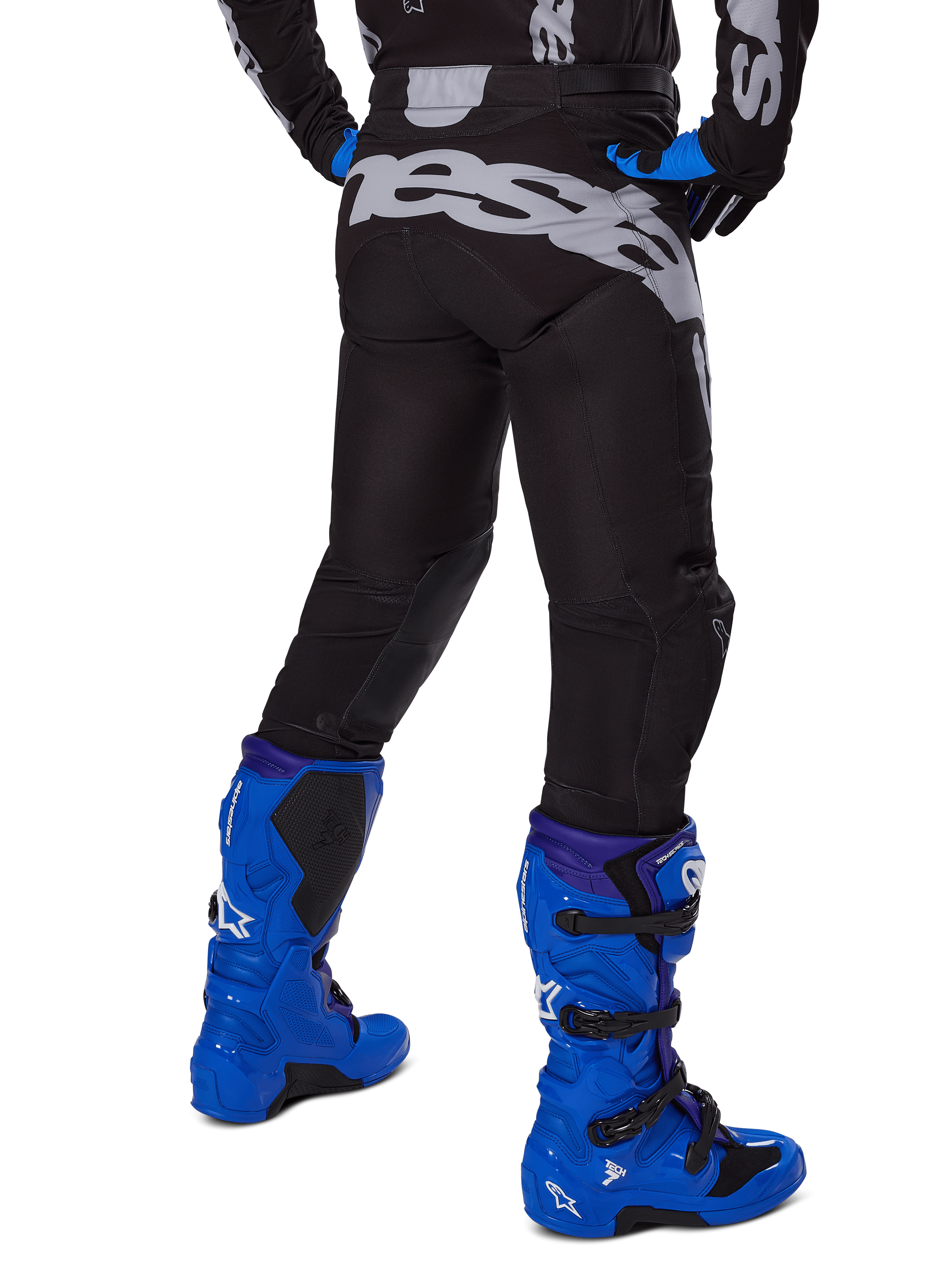Alpinestars 2025 Racer Graphite Pants, pantalon de motocross, noir et gris, vue arrière avec un grand logo gris sur l'assise, porté avec des bottes de motocross bleu vif et un maillot noir et bleu, équipement de course tout-terrain durable