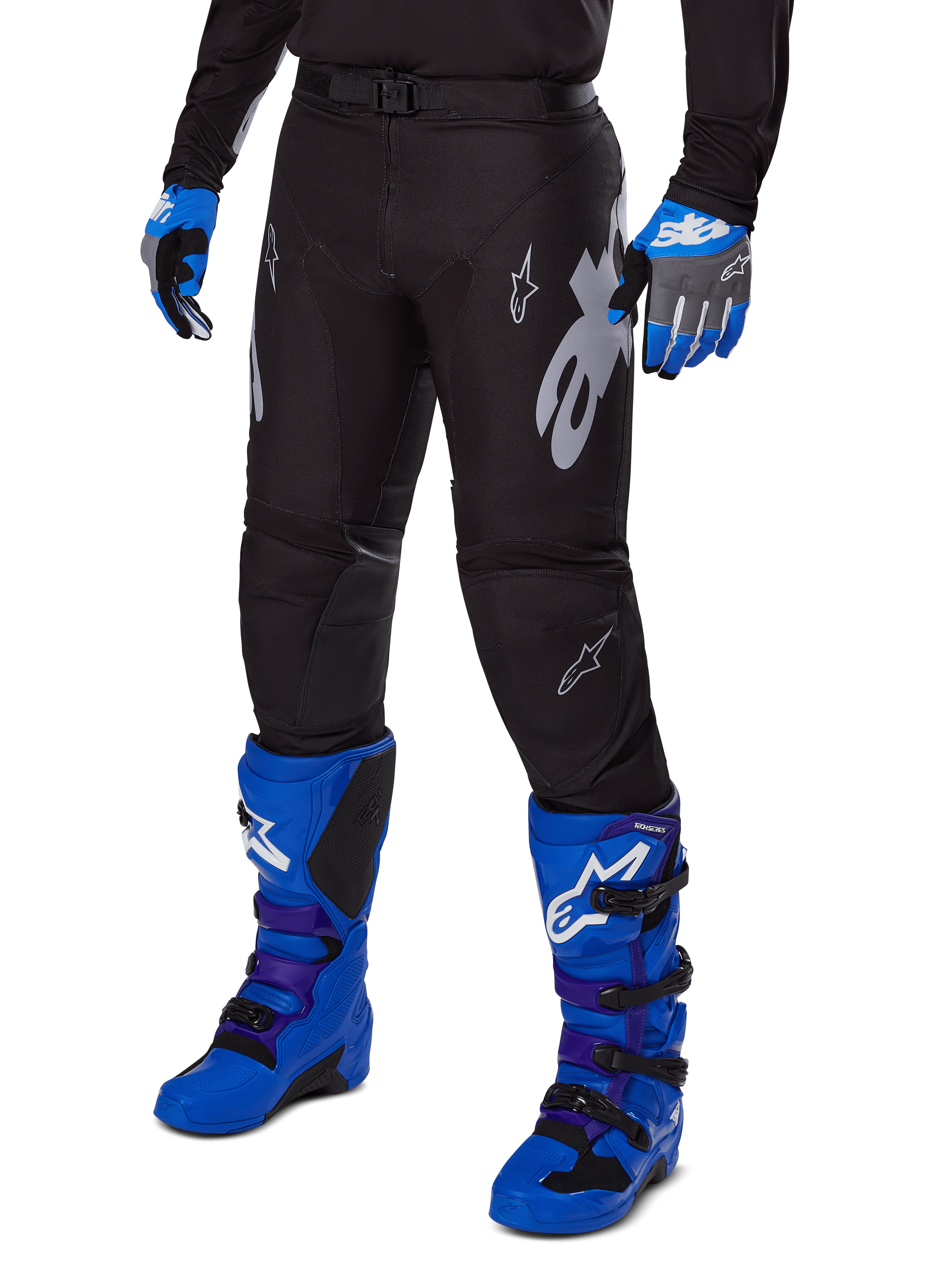 Pantalon Alpinestars Racer Graphite 2025, pantalon de motocross noir avec graphismes blancs et gris, porté avec des bottes de motocross bleu vif et des gants bleus assortis, tissu technique durable pour la conduite tout-terrain