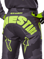 Alpinestars 2025 Racer Hollow broek, motorcross broek, Dark Camo en fluorgeel, met een groot geel Alpinestars-logo op de achterkant, tactisch camouflagepatroon met felgele accenten en een duurzame constructie voor off-road racing.
