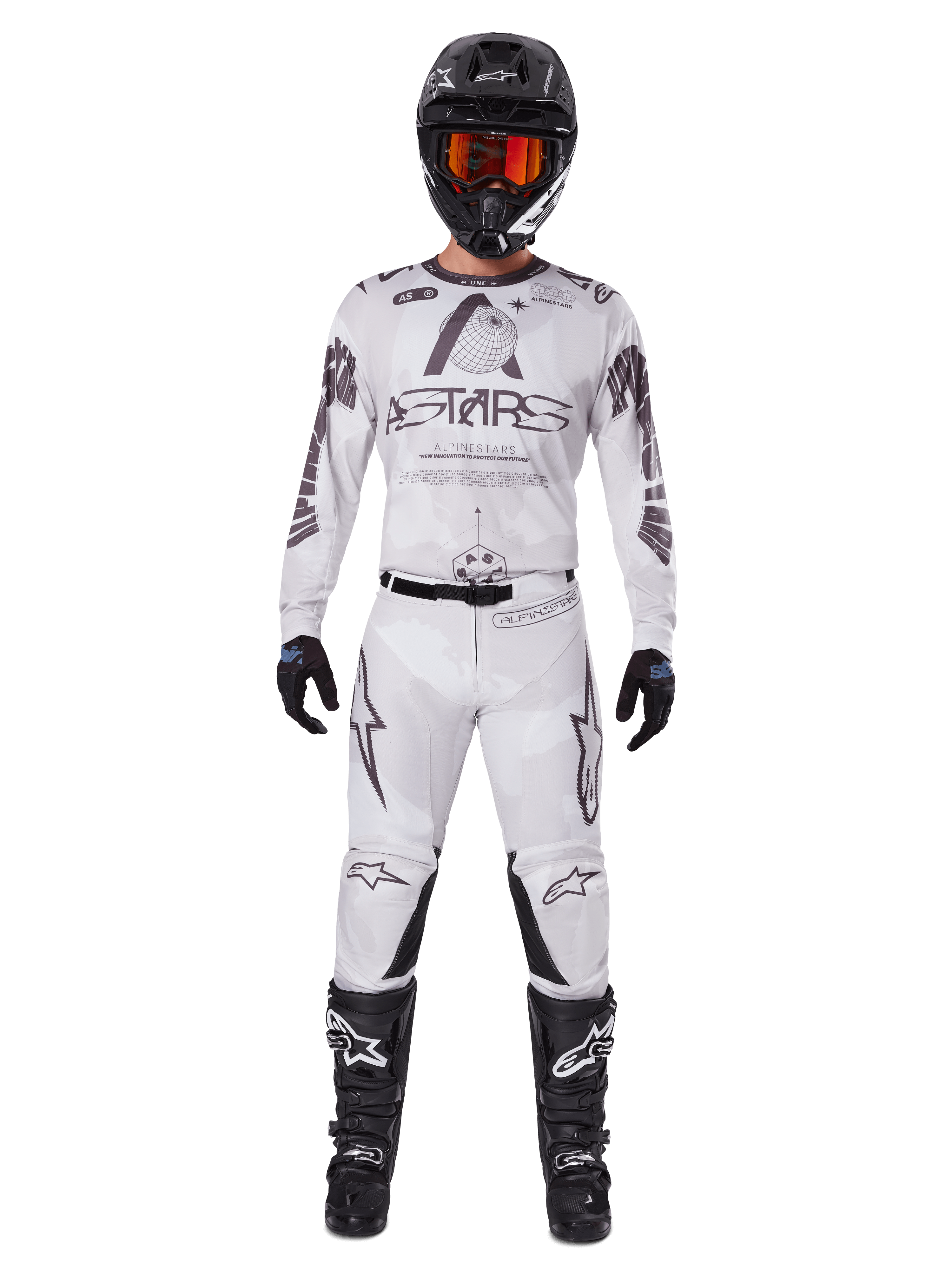 Motorcrossrijder in Alpinestars 2025 Racer Hollow crossbroek in Light Camo Brown, gecombineerd met een bijpassend wit en grijs shirt met lange mouwen, zwarte helm met oranjerode bril, zwarte handschoenen en zwarte laarzen, gecoördineerde race-uitrusting voor off-road prestaties.