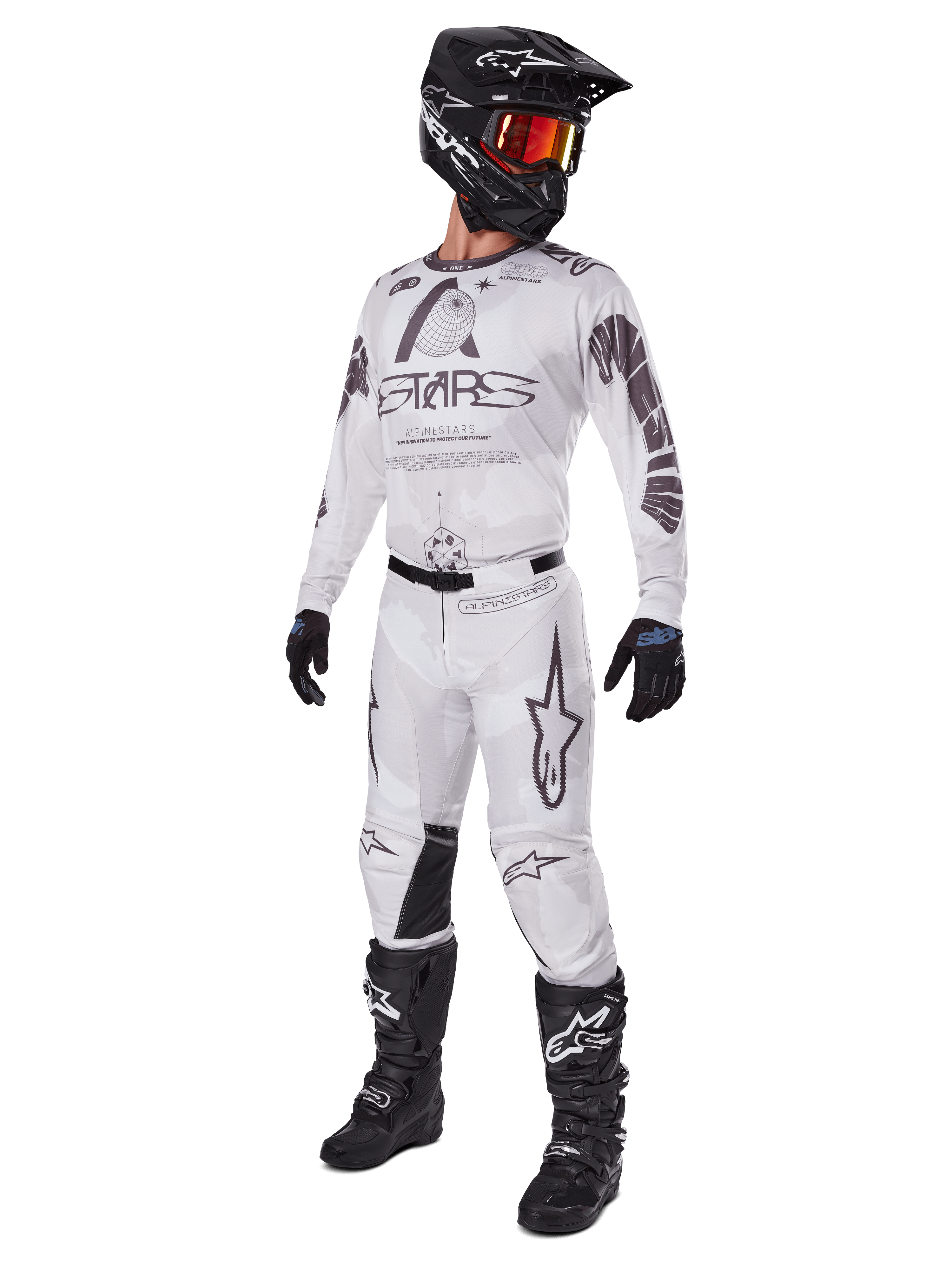 Alpinestars 2025 Racer Hollow broek, motorcross broek, lichtbruine camouflage, getoond als onderdeel van een complete race-uitrusting met een wit shirt, zwarte helm en zwarte laarzen, voorzien van versterkte zwarte kniepanelen en een subtiel camouflage-ontwerp.
