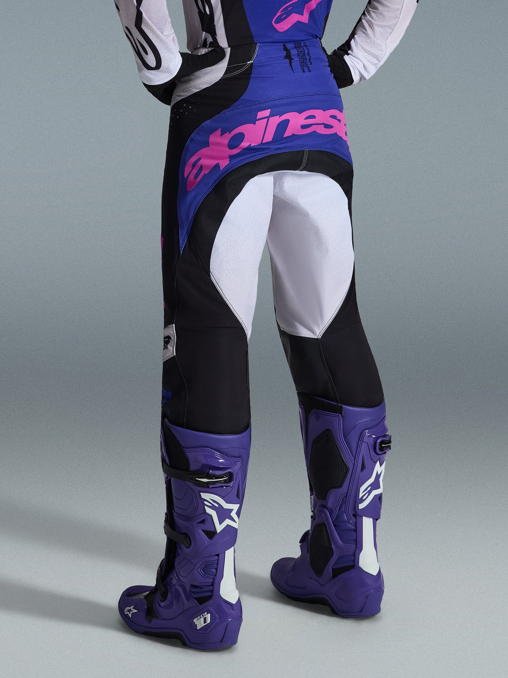 Alpinestars 2026 Techstar Knif Hose, Motocross-Hose, Schwarz, Hellgrau und Lila, Rückansicht mit pinkem Branding auf dem Gesäß, getragen mit passendem Trikot und lila Motocross-Stiefeln, professionelles Offroad-Rennoutfit