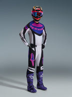 Motocross rider wearing the Alpinestars 2026 Techstar Knif Gear Set, white jersey with black, blue, and pink accents, matching pants with pink Astars logos, multi-colored helmet with goggles, purple racing boots, coordinated high-performance gear for motocross competition