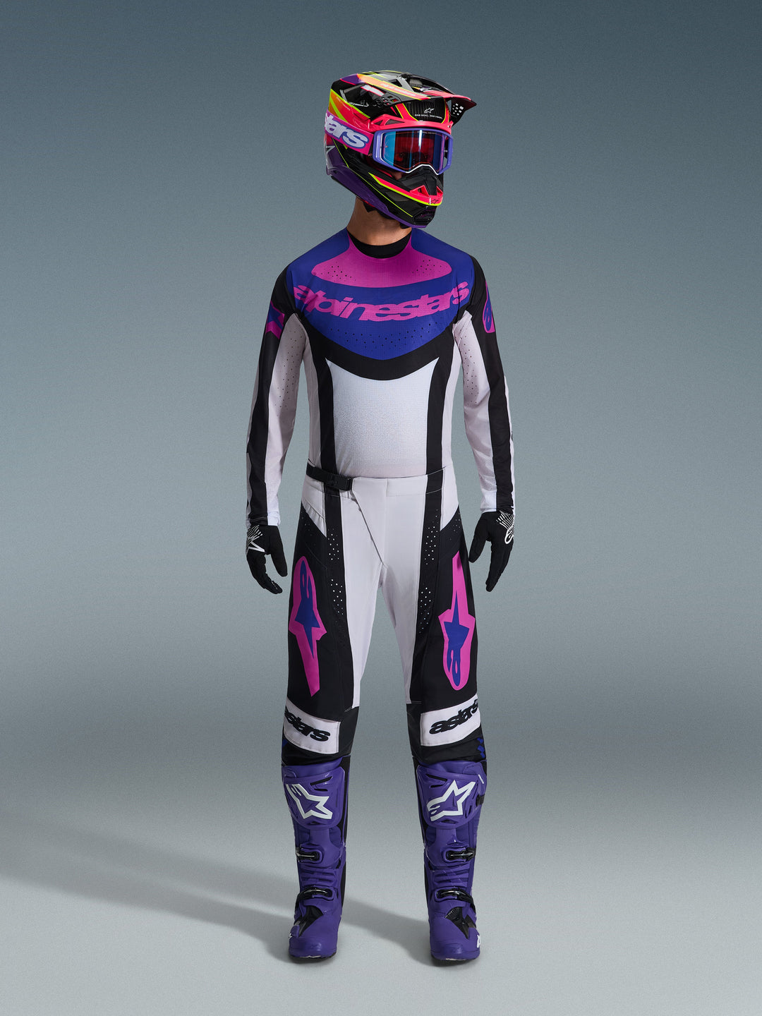Alpinestars 2026 Techstar Knif Gear Set, tenue de motocross complète, blanc, noir, violet et rose, portée avec un casque multicolore, des lunettes bleues, des bottes violettes et des gants noirs, équipement haute performance coordonné pour la course tout-terrain