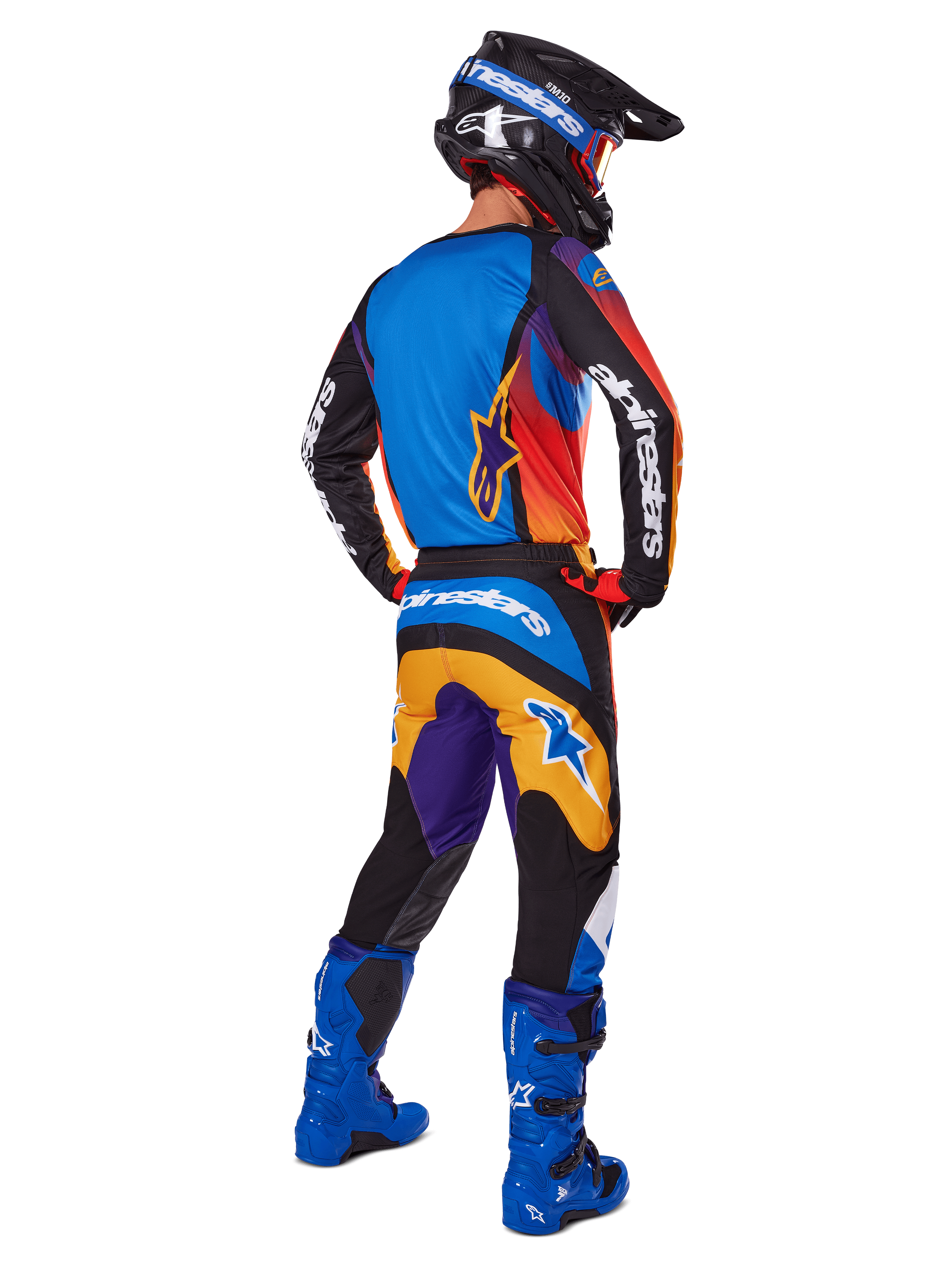 Motocross-Fahrer von hinten in der Alpinestars 2025 Fluid Wurx Hose, mehrfarbiges Design mit blauen, orangefarbenen, gelben und lila Akzenten, kombiniert mit einem passenden Trikot, leuchtend blauen Stiefeln und schwarzem Helm, komplette Offroad-Rennausrüstung.