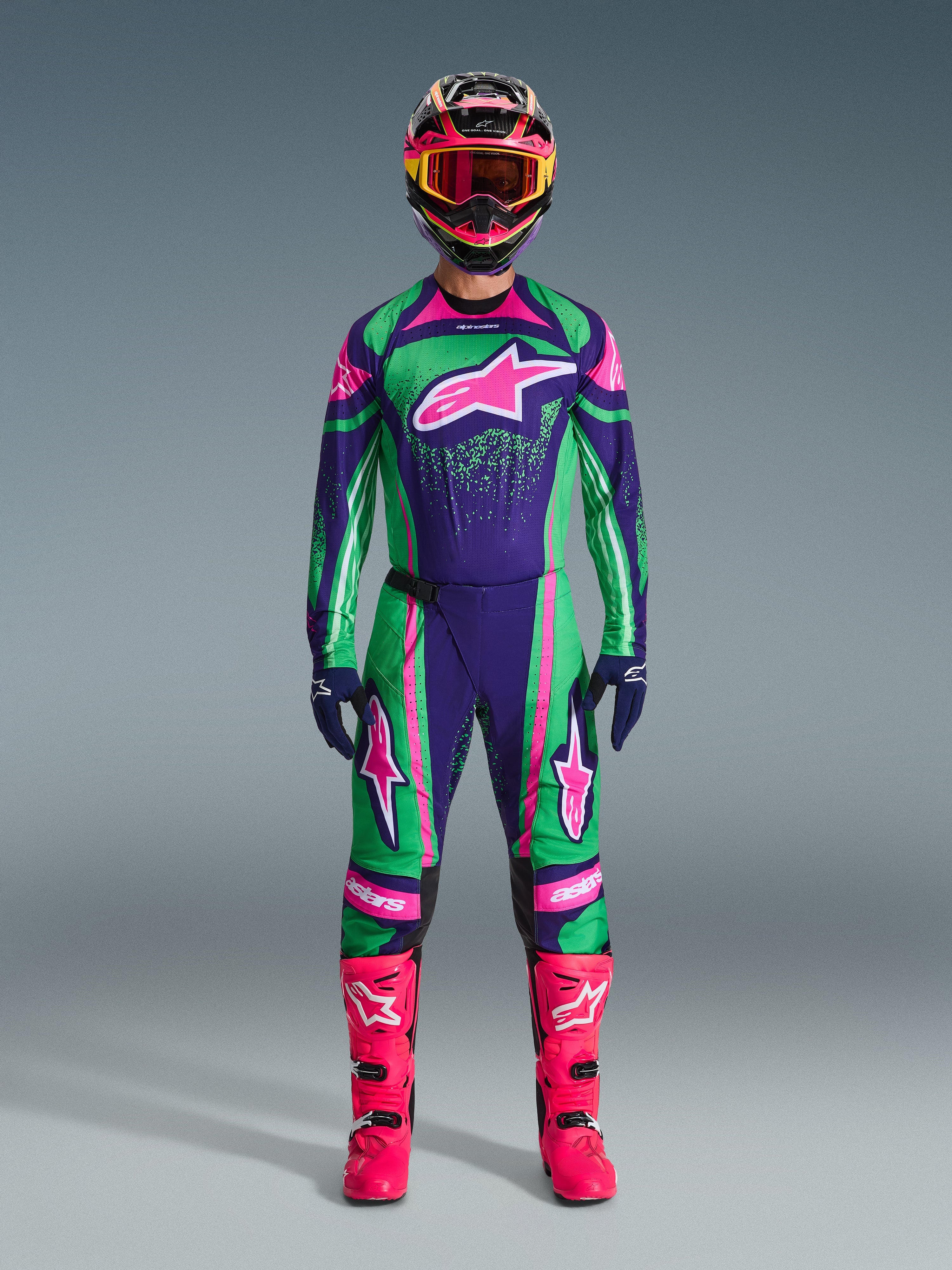 Alpinestars 2026 Techstar Nomur Gear Set, tenue de motocross, vert, violet et rose éclatant, grand logo étoile sur la poitrine et les cuisses, casque noir avec détails roses et jaunes, bottes rose vif, design sportif professionnel